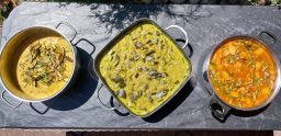 Linsen Curry, Auberginen-Kartoffel-Bohnen Curry Drei Töpfe mit verschiedenen Currys auf einem schwarzen Steintisch.