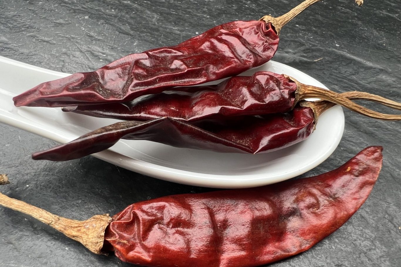 Chilli Ein Löffel mit einem Haufen Chilli-schoten und einer davorliegenden Chilli-schote.